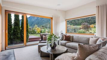 Un salon moderne comprenant un canapé, un fauteuil et une table basse, de grandes portes-fenêtres coulissantes et une vue sur un paysage montagneux.