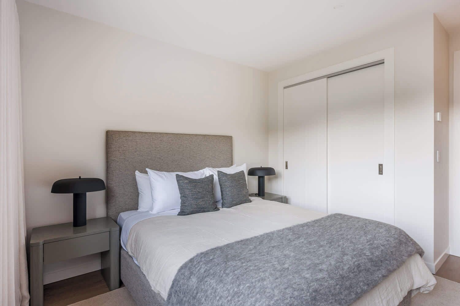 A bedroom with a bed, two bedside tables, a wardrobe, and a door.