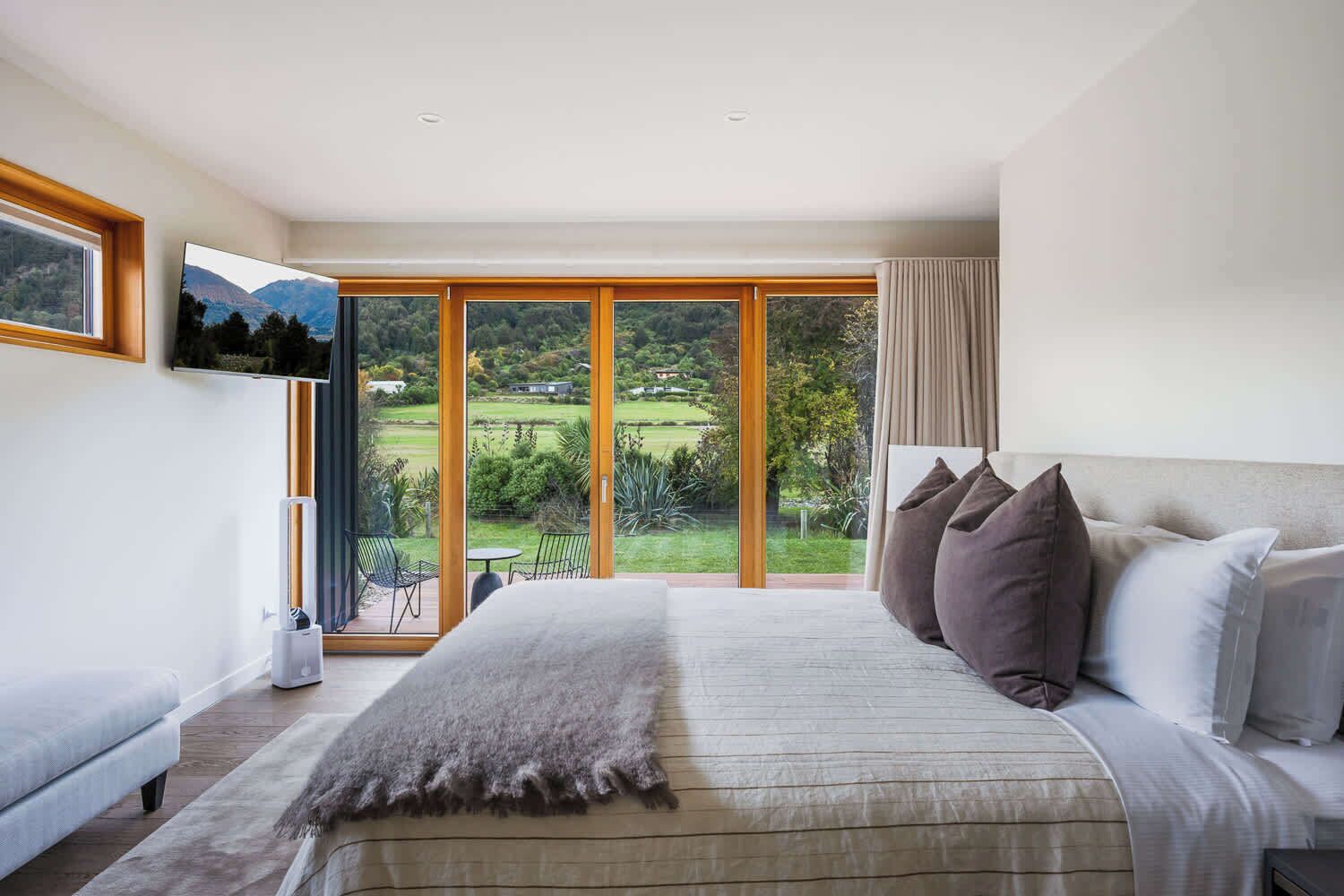 Une chambre avec un grand lit, une télévision et une vue sur un jardin et des montagnes.