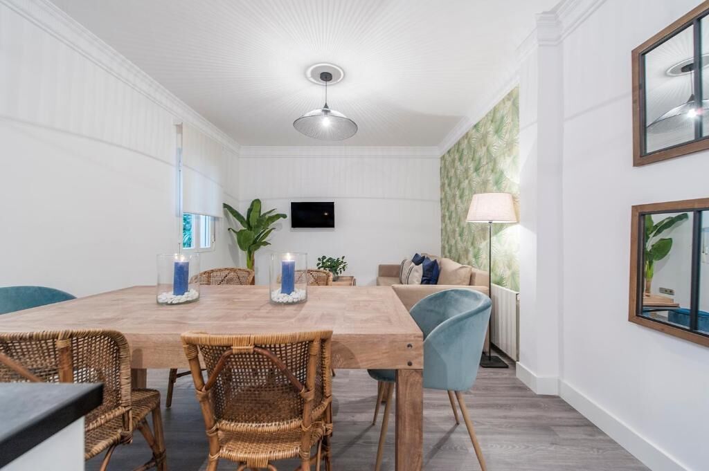 A dining area with a wooden table, wicker chairs, a TV, and a lamp.