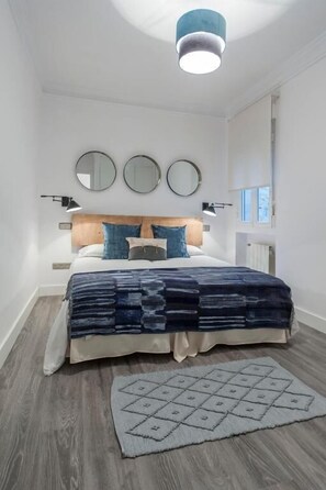 A bedroom with a bed, bedside lamps, a rug, and a ceiling light. - Zurbano (Madrid)