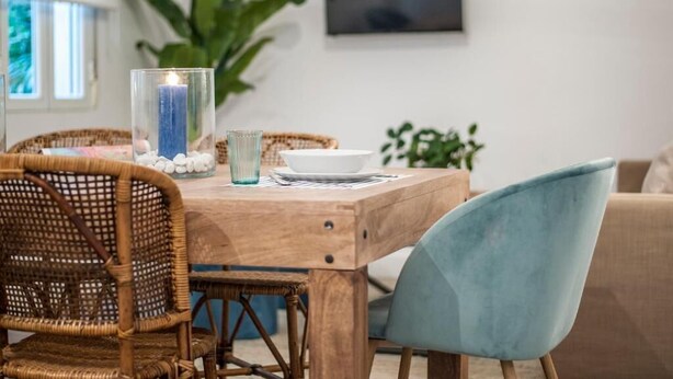 Ein Essbereich mit einem Holztisch, Korbstühlen, einem Kerzenhalter aus Glas und einem blauen Sessel.