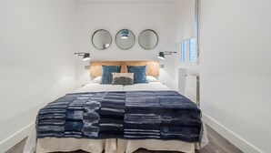 Ein Schlafzimmer mit einem Bett, einem Kopfteil, drei Wandspiegeln und einem Fenster.