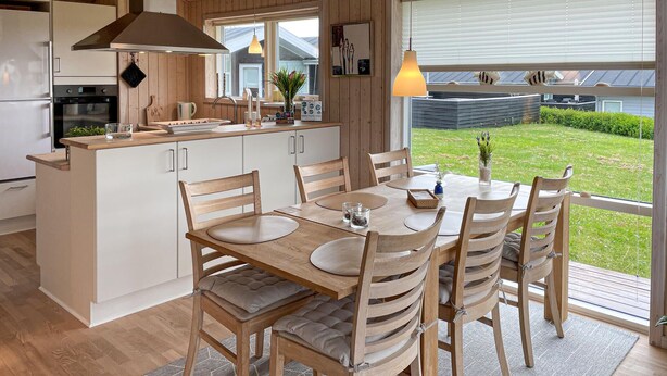 Una cocina moderna con comedor, muebles de madera y vistas a un jardín.
