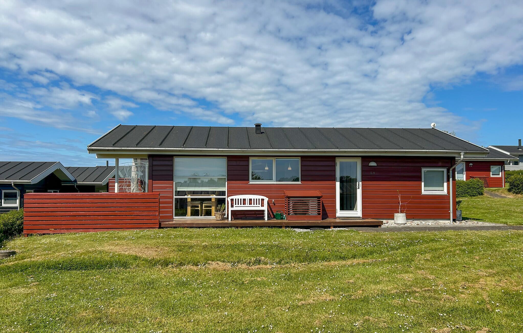 Een rood huis met één verdieping, een zwart dak, een voortuin met een bankje en een kleine tuin.