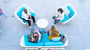 Un gruppo di persone sedute su un divano blu da esterno, con un tavolo bianco al centro, su un pavimento piastrellato.