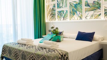 Habitación de hotel con cama, almohadas, una planta decorativa y una ventana con vista a hojas de palmera.