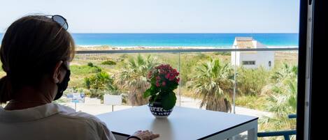 A person seated at a table with a view of the sea and a white building in the distance.