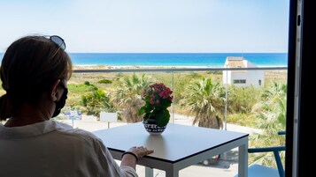 Una persona sentada en una mesa con vista al mar y un edificio blanco a lo lejos.