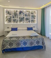 Un dormitorio moderno con una cama grande, un ventanal con diseño de hojas tropicales y vistas al exterior.