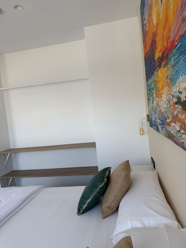 Una camera da letto con un letto, cuscini, un quadro e scaffali a muro.