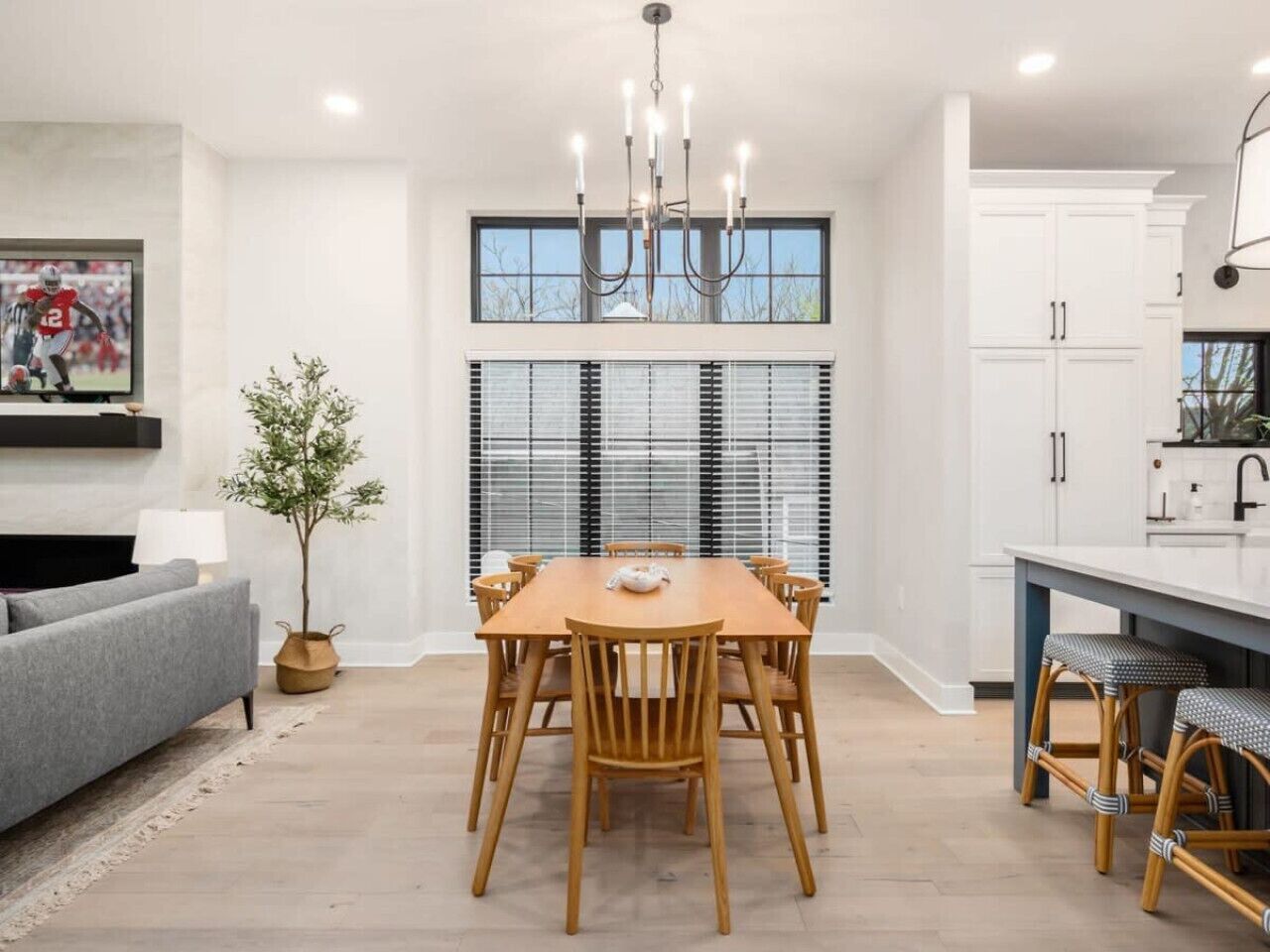 A modern kitchen with white cabinets, a dining table with chairs, a grey sofa, and a chandelier.