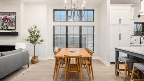 Eine moderne Küche mit weißen Schränken, einem Esstisch mit Stühlen, einem grauen Sofa und einer Chandelier.