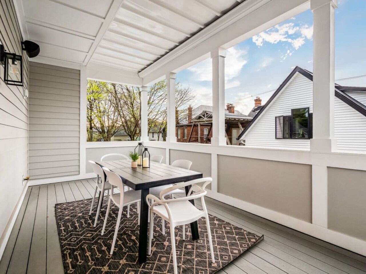 A covered patio with a table and chairs, a patterned rug, and a view of neighboring houses.