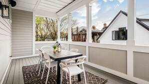 Eine überdachte Terrasse mit Tisch und Stühlen, einem gemusterten Teppich und Blick auf angrenzende Häuser.