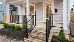 Ein zweistöckiges Haus mit überdachter Veranda, der Hausnummer '245' an der Haustür und einem kleinen Garten mit Sträuchern.