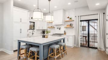 A modern kitchen with white cabinets, a central island with bar stools, pendant lighting, and a view to a balcony.