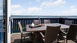 Eine Terrasse mit Korbstühlen und einem Tisch, mit Blick auf ein Gewässer.
