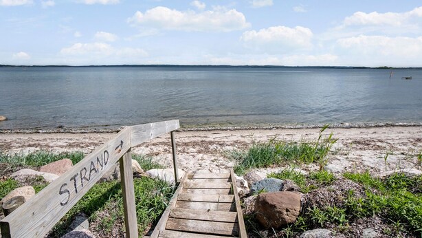 Eine Holztreppe führt zu einem Strand, auf dem ein Schild 'STRAND' steht.