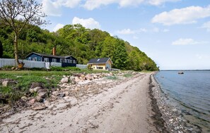 A beachside property with a dirt path leading to a small house, surrounded by a white fence and lush greenery.