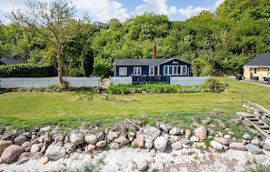 A blue house with a white fence, surrounded by a grassy yard and a stone wall.