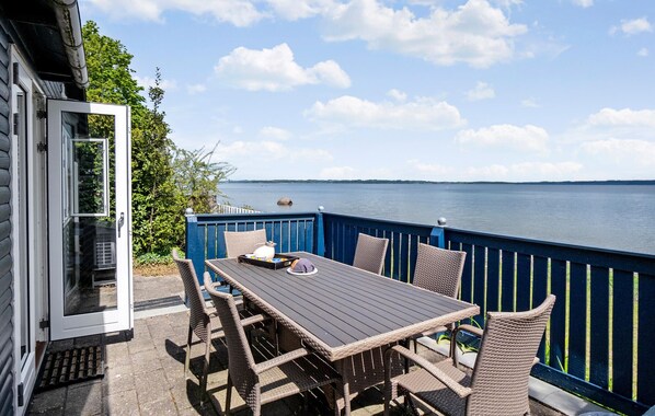 A patio with a table and chairs, a view of the water, and a blue fence.