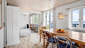 Ein Essbereich mit Holztisch, Stühlen, einem weißen Schrank und Meerblick durch große Fenster.