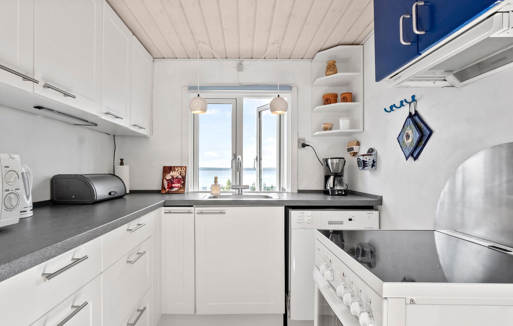 Een moderne keuken met witte kastjes, een ingebouwde vaatwasser, een koffiezetapparaat en uitzicht op de omgeving.