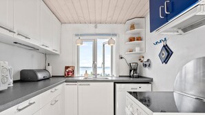 Eine moderne Küche mit weißen Schränken, einem eingebauten Geschirrspüler, einer Kaffeemaschine und Blick ins Freie.