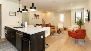 Eine moderne Küche mit Kochinsel, ein Essbereich mit Sofa und Stühlen, ein Wohnzimmer mit Couchtisch und Stühlen sowie ein großes Fenster mit Jalousien.