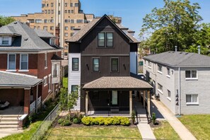 A two-story residential building with a dark exterior, a covered front porch, and a small garden area.