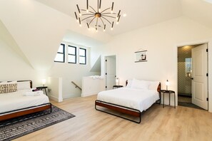 A modern bedroom with two beds, a chandelier, a staircase, and a view of the outdoors.