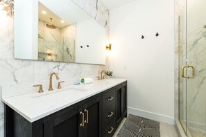 A bathroom with a marble vanity, a large mirror, a shower with glass doors, and a black and white patterned rug.