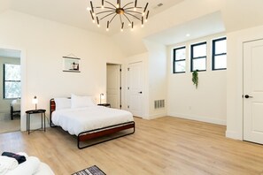 A modern bedroom with a bed, bedside tables, a hanging plant, and a ceiling light fixture.