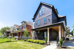 A modern two-story residential building with a dark exterior, multiple windows, and a covered front porch.