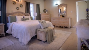 A bedroom with a large bed, a dresser, a vanity with a mirror, and a fluffy rug. - Exquisite 3-bedroom house in peaceful Mount Pleasant, St. John’s with AC comfort (St. John’s)