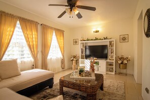 Ein Wohnzimmer mit einer Couch, einem Couchtisch, einem Fernseher und einem Deckenventilator.
