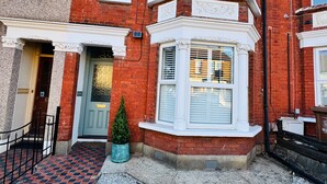 A red brick building with a bay window, a door with a number plate, and a small potted plant. - Designer 2 Bedroom Apartment in London with Garden (Bexleyheath)