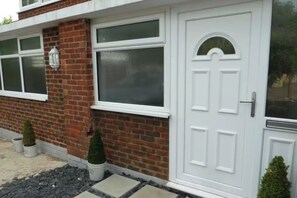 A house with a white front door, a brick facade, and two small potted plants. - Studio Sleeps 2 - Pets Welcome - Enclosed Garden (Bognor Regis)