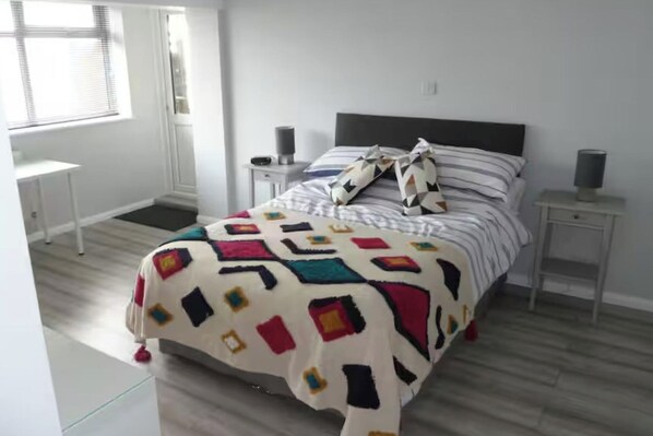 A bedroom with a bed, bedside tables, a window, and a door. - Studio Sleeps 2 - Pets Welcome - Enclosed Garden (Bognor Regis)