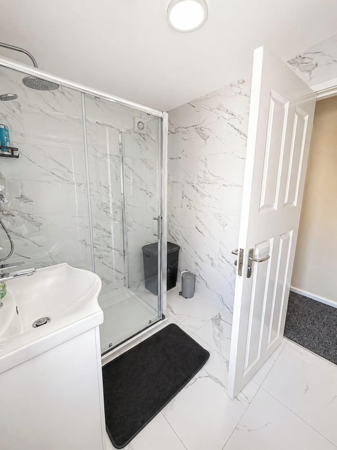 A bathroom with a glass-enclosed shower, a white sink, and a marble-tiled floor.
