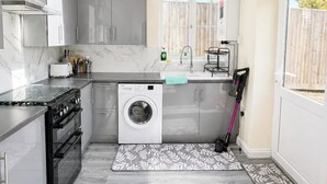 Een compacte keuken met een ingebouwde wasmachine, dakraam en een rode emmer.