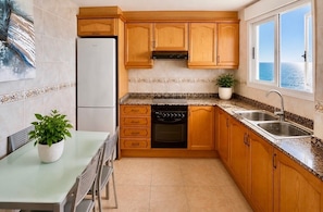 Una cucina compatta con mobili in legno, forno a incasso, lavastoviglie e una finestra vista mare.