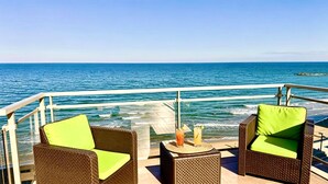 A deck with wicker chairs and a table, overlooking the ocean.