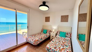 A bedroom with two beds, a balcony with a view of the sea, and a ceiling light.