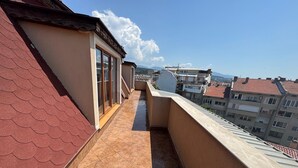 A narrow balcony with a tiled floor, a red roof, and a view of surrounding buildings. - Apartment Sleeps 6- Free Parking- Balcony (Казанлък)