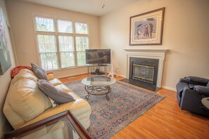 A living room with a sofa, a glass coffee table, a fireplace, and a television. - Enjoyable 3-bedroom house with great yard in charming South Durham (Durham)
