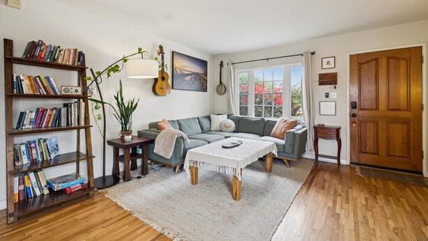 A living room with a sectional sofa, a coffee table, a bookshelf, a guitar, and a door. - Santa Cruz Beach Bungalow | Walk to Beach | Garden (Santa Cruz)