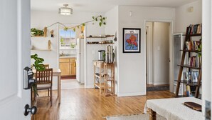 A modern living room with a wooden floor, a dining area with a table and chairs, a bookshelf, and a kitchen visible through an open door. - Santa Cruz Beach Bungalow | Walk to Beach | Garden (Santa Cruz)