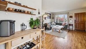 A cozy living space with a wooden coffee table, a sofa, a kitchen area with a kettle and a coffee maker, and a wine rack. - Santa Cruz Beach Bungalow | Walk to Beach | Garden (Santa Cruz)
